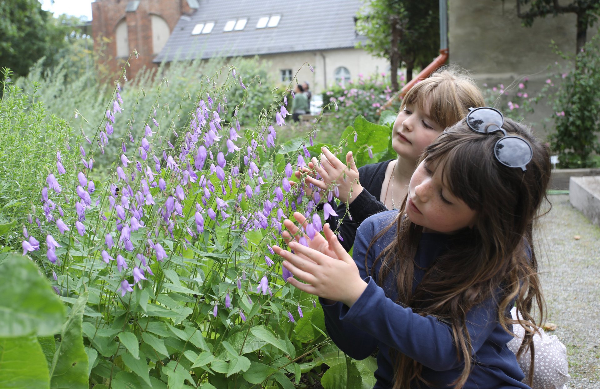 Dwie dziewczynki podziwiają dzwonki w ogrodzie klasztornym.