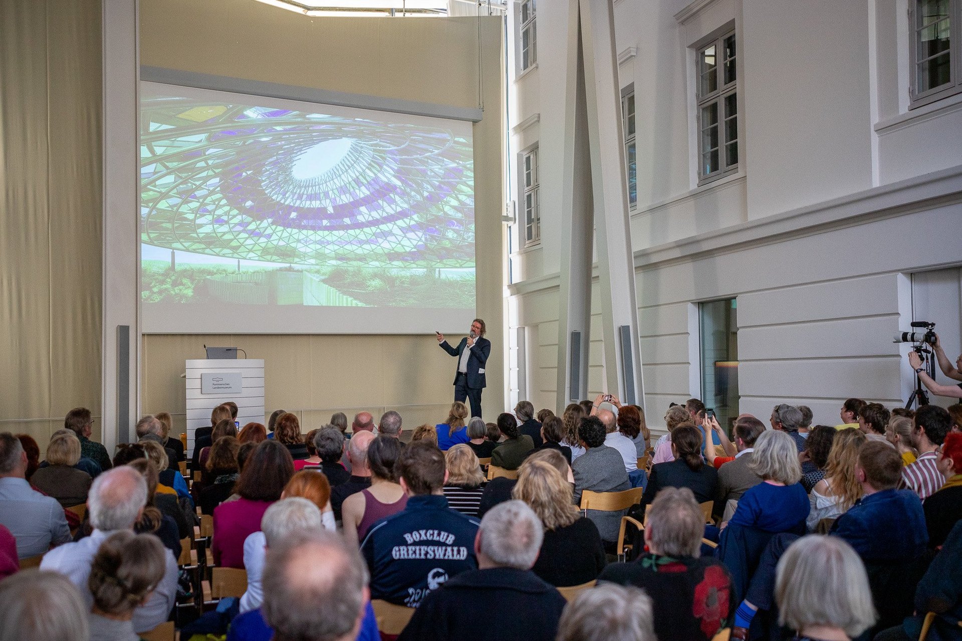 Olafur Eliasson beim Artist Talk: vorn Publikum, dahinter der Referent mit Präsentation.