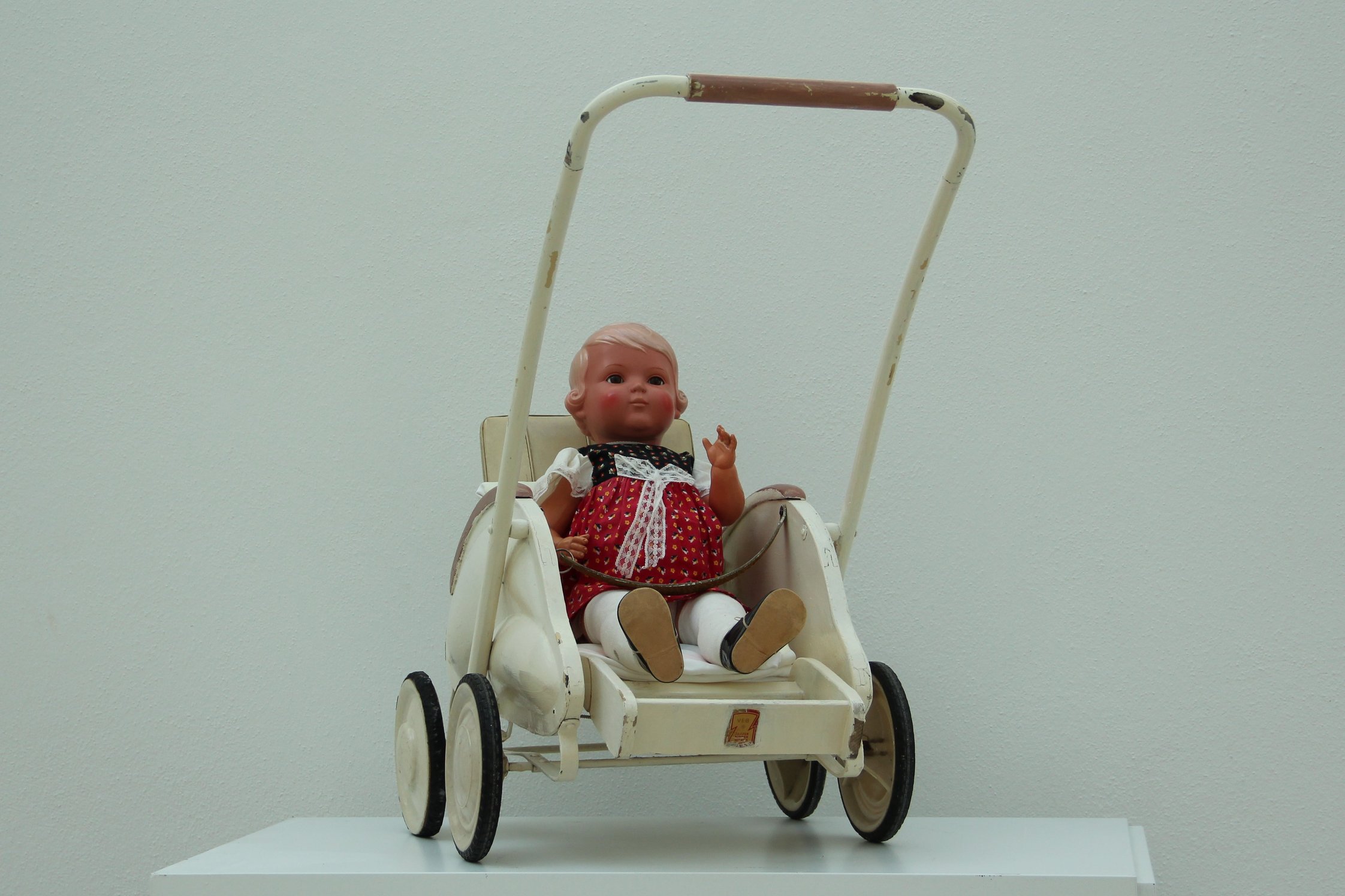 Schildkröt-Puppe „Inge“ sitzt in einer Puppen-Sportkarre der ZEKIWA. Sie trägt ein geblümtes Kleidchen mit einer großen Schleife.
