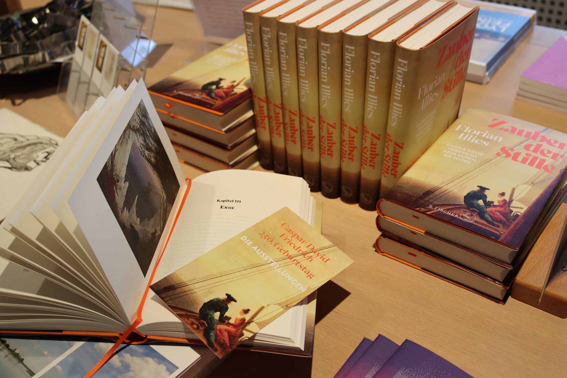 Florian Illies, „Zauber der Stille“: Ein Buch ist aufgeschlagen, im Hintergrund stehen und liegen weitere Exemplare des Buchs.
