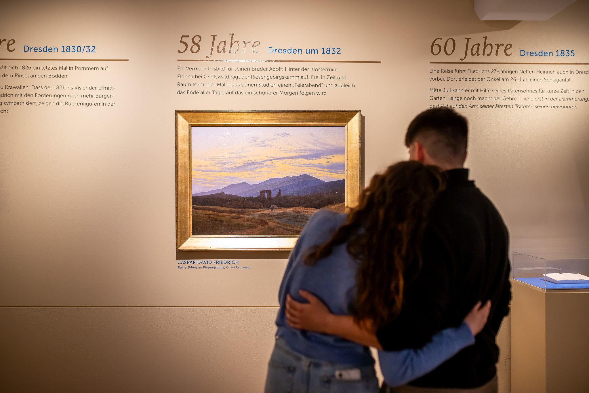 Ein sich umarmendes Paar betrachtet das Gemälde „Ruine Eldena im Riesengebirge“.