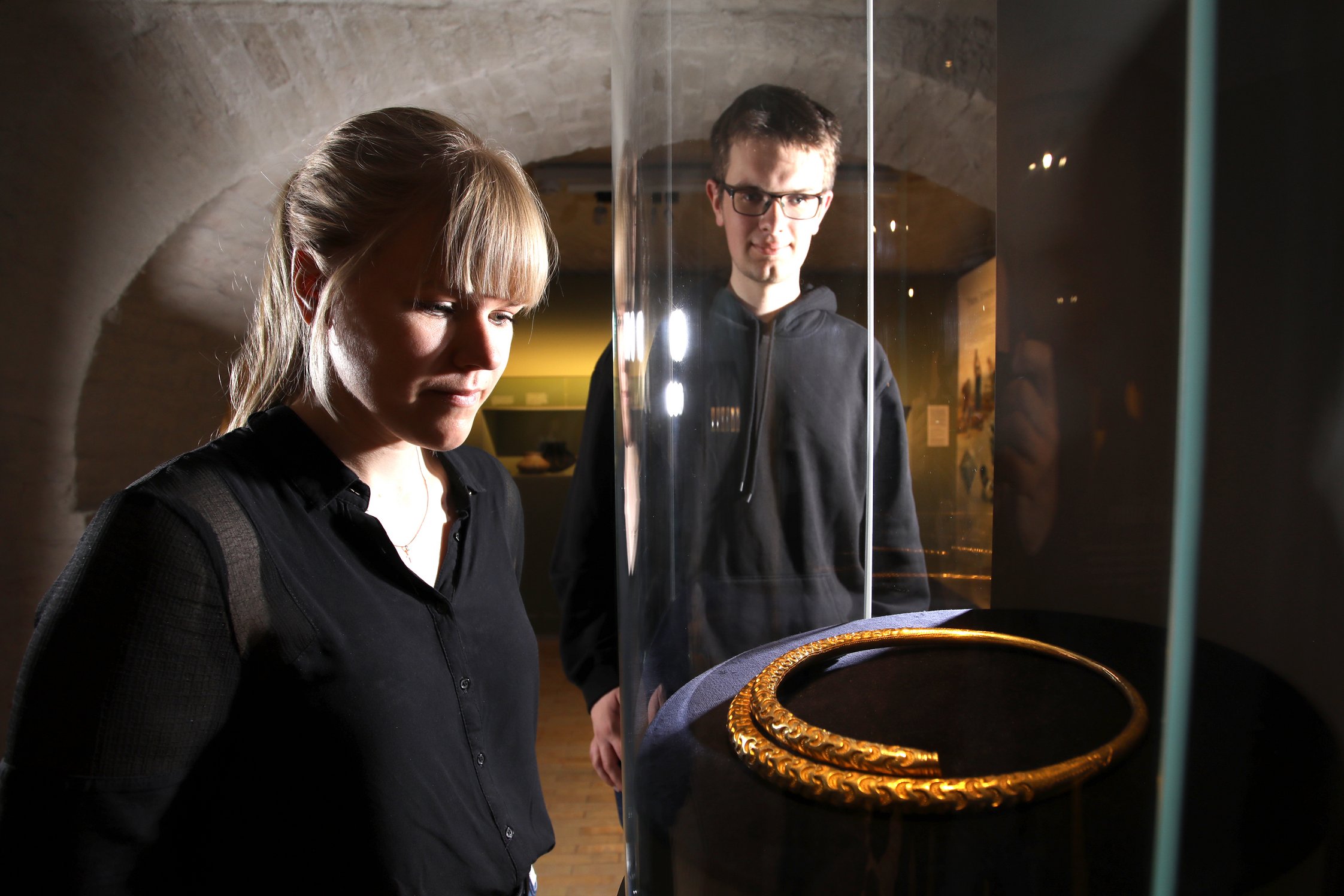 Zwei Besucher*innen betrachten den goldenen Halsring von Peterfitz, der in einer Vitrine liegt. Foto: Vincent Leifer