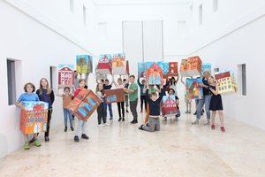 Presentation of the project in the atrium of the museum: young students hold up large colourfully painted cubes.