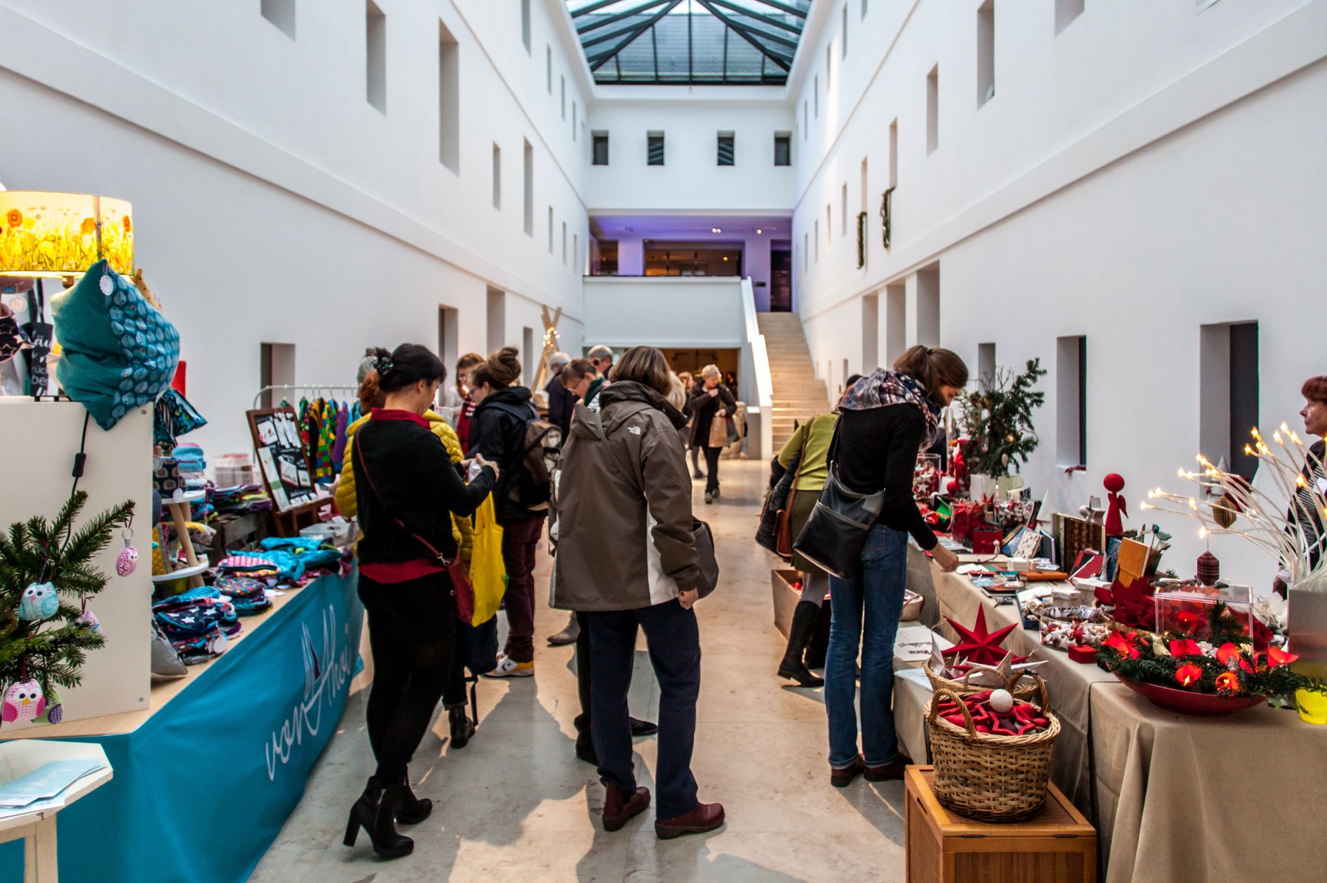 Kunsthandwerkermarkt: Blick in den Lichthof. Mehrere Stände mit weihnachtlichen Waren und Kunsthandwerk, dazwischen Besucherinnen und Besucher. Foto: Henry Dramsch