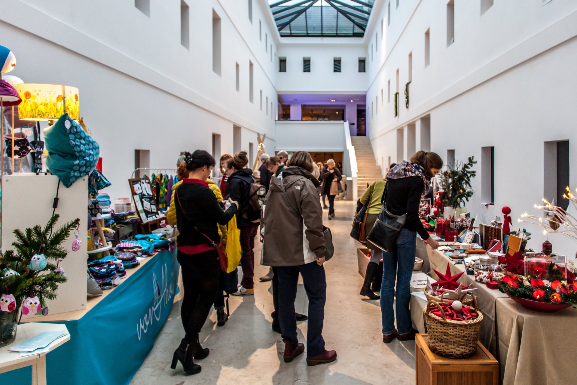 Kunsthandwerkermarkt: Blick in den Lichthof. Mehrere Stände mit weihnachtlichen Waren und Kunsthandwerk, dazwischen Besucherinnen und Besucher. Foto: Henry Dramsch