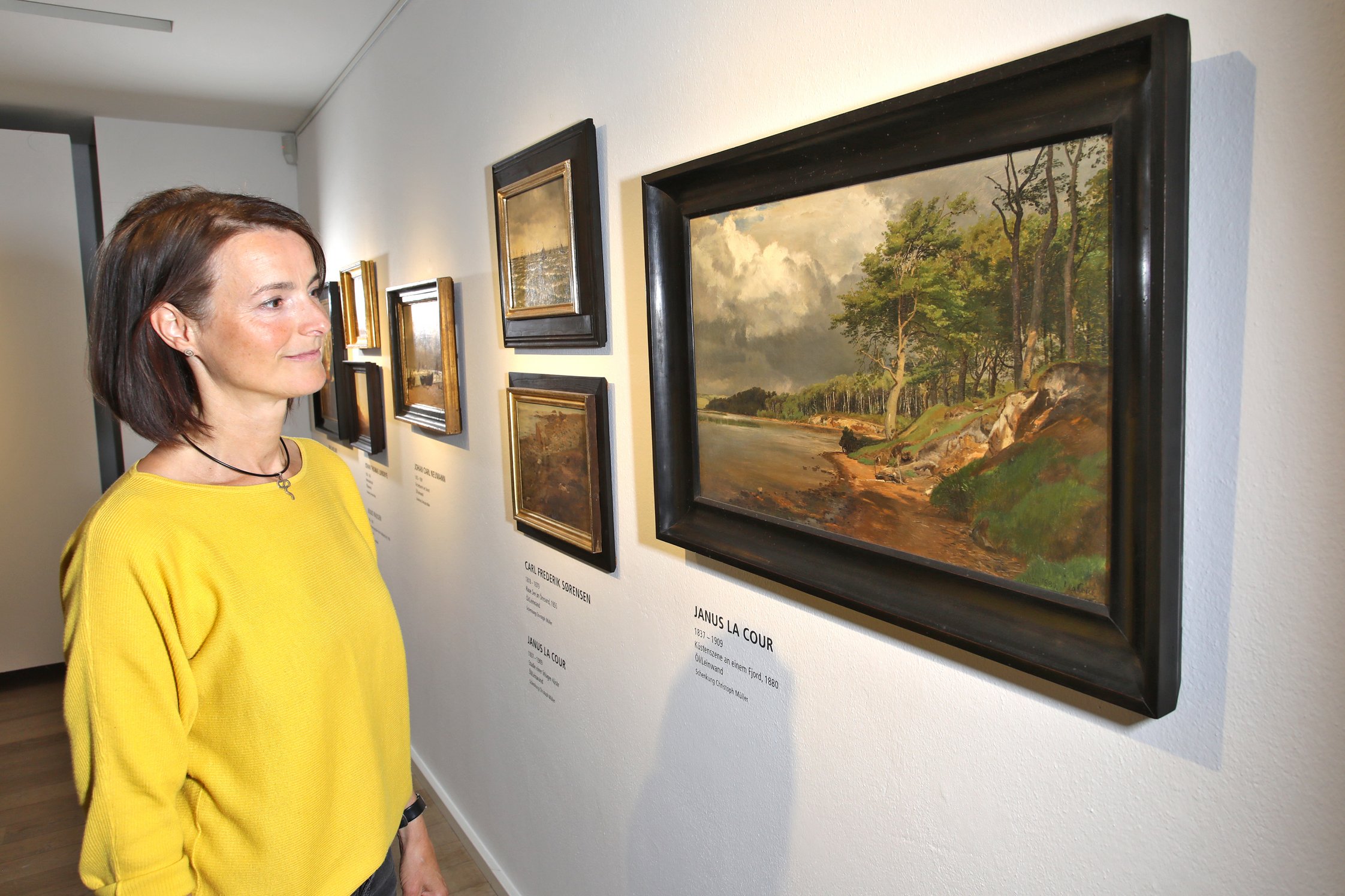 Eine Besucherin betrachtet einige Gemälde dänischer Künstler aus dem 19. Jahrhundert, darunter Janus La Cour.