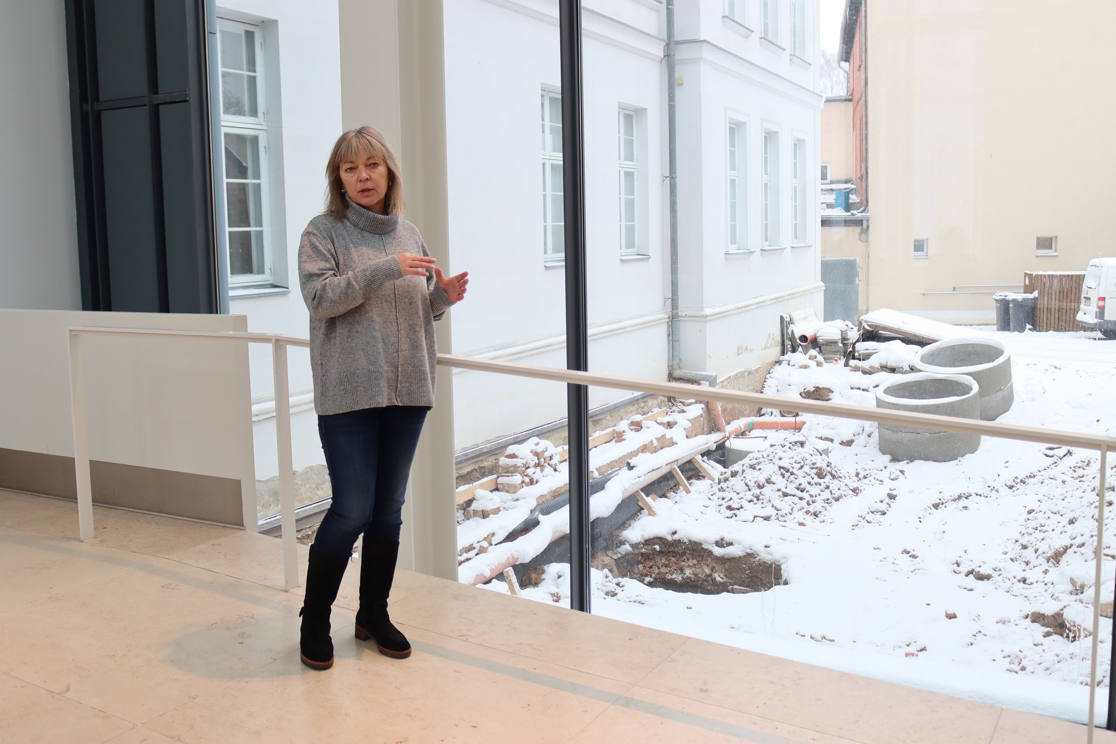 Ausgrabungsleiterin Renate Samariter steht in der Museumsstraße. Durch große Glasfenster sieht man die eingeschneite Ausgrabungsfläche.